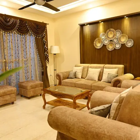 Traditional living room with swagged drapery, a dark walnut-panelled feature wall lit by spotlights above a sunburst metal wall-art cluster