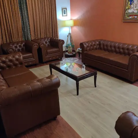 Traditional living room with tufted brown leather Chesterfield sofas and armchairs around a glass-top wood coffee table against an orange textured wall.