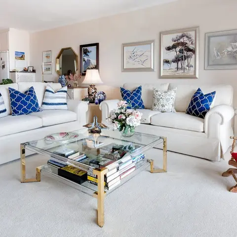 Traditional living room with two cream slipcover sofas piled with navy patterned pillows, a glass-and-brass coffee table