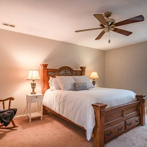 Traditional master bedroom with a carved wood queen bed, matching nightstands with table lamps, a wood rocking chair with a throw, and a five-blade ceiling fan.