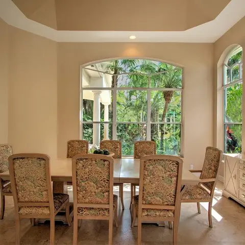 Traditional villa dining room with a tray ceiling, arched windows framing palm trees and a floral-upholstered 8-seat dining set