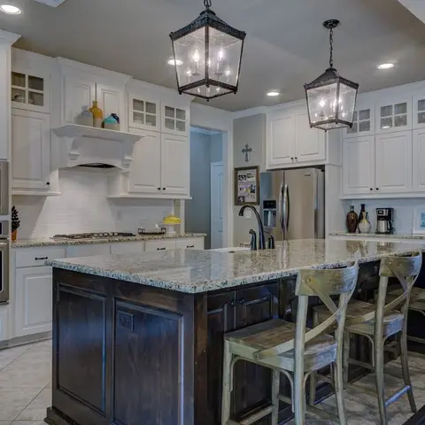 Traditional white kitchen with glass-front upper cabinets, a dark wood granite-topped island with bar stools and twin lantern pendants