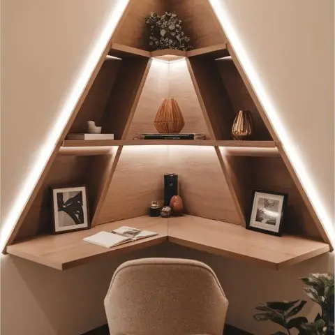 Triangular oak corner desk-and-shelf unit outlined in a continuous LED strip, with a boucle chair and one open book on the worktop