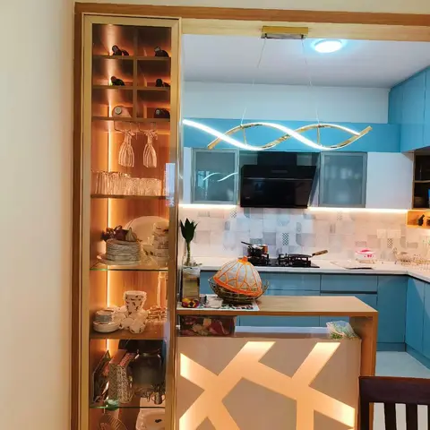 Turquoise modular kitchen with a backlit geometric jaali panel on the breakfast counter and a lit glass-front crockery display unit.