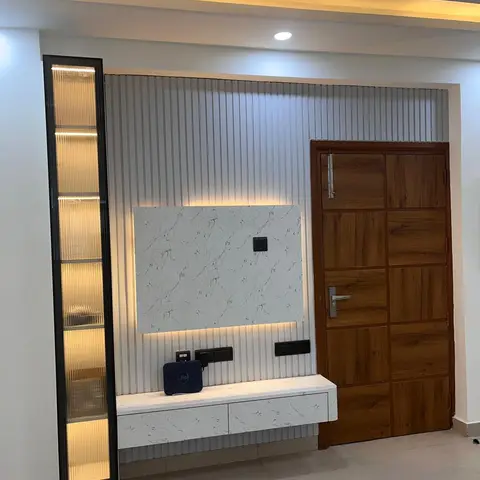 TV console wall with fluted PU-finish panelling, a backlit marble display niche, and a floating white marble-top console, beside the panelled wooden main door.