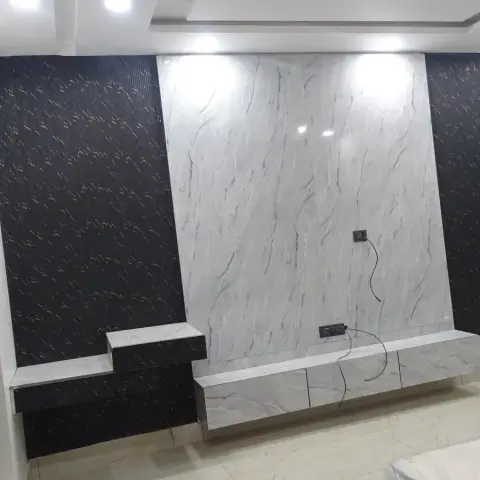 TV feature wall combining book-matched white marble with black textured wall panels and a floating marble console, still mid-installation with exposed wiring.
