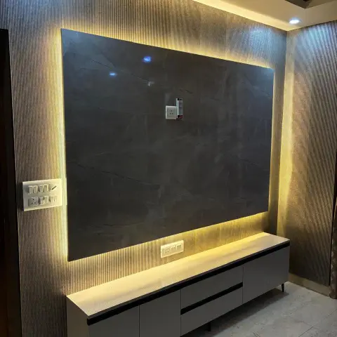 TV feature wall with a backlit dark stone slab panel framed by fluted wall panelling and a floating grey console below.