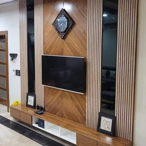 TV feature wall with a herringbone wood-grain panel behind a diamond-shaped wall clock and TV, flanked by vertical fluted panelling with inset mirror strips