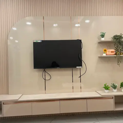 TV feature wall with an arched glossy panel edged in rose-gold inlay strips above a floating cream TV console