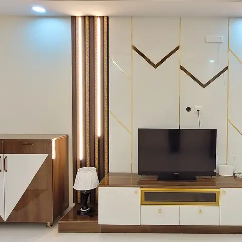 TV feature wall with gold-inlaid chevron panelling flanked by backlit fluted wood pilasters, paired with a brass-trimmed glossy TV console.