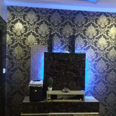 TV media wall with bold navy-and-gold damask wallpaper and dark marble-look panelling behind the unit, lit by blue LED accent lighting along the edges.