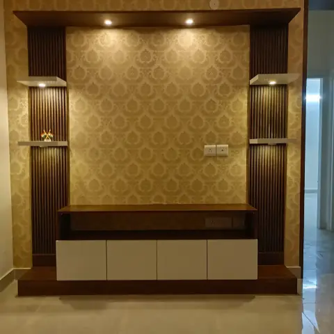 TV unit built against gold damask wallpaper, with dark fluted side panels, two pairs of spotlit white floating shelves and a white-shuttered console on a wood