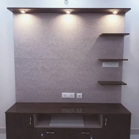 TV unit wall with a dark stone-textured backdrop, three asymmetric floating shelves, ceiling spotlighting