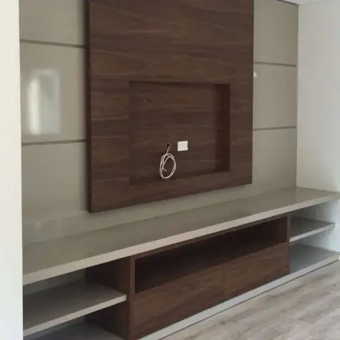TV unit wall with a recessed wood-panel niche framed by taupe panelled walls, over a floating stone-top console with open shelving and a wood-laminate drawer