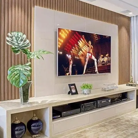 TV wall combining fluted wood side panels with a glossy cream center panel, above a long floating console styled with a monstera leaf arrangement and ginger