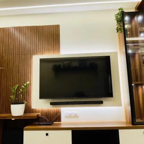 TV wall in a flat's living room: fluted teak-finish panelling to the left of a backlit white recess holding the screen and soundbar