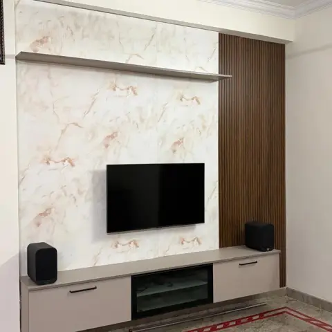 TV wall in an older flat - glossy peach-veined marble-print panel with a floating shelf and wall-hung beige console, a fluted teak panel to the right