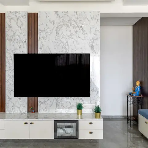 TV wall in white marble slab split by two teak fluted strips, a white console with brass capsule handles and a reeded-glass centre door