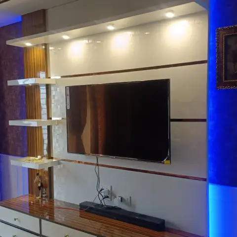 TV wall photographed at night with blue LED wash on the right return, a high-gloss white and teak-veneer console with crystal-knob drawers