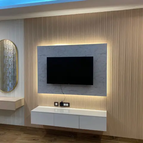 TV wall with backlit marble-look panel set into fluted wood cladding, a floating gloss console and an oval brass-framed mirror over a side console