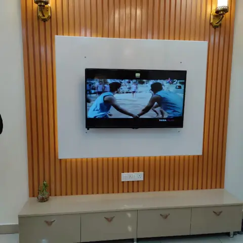 TV wall with orange fluted wood panelling and brass wall sconces, above a cream drawer console with V-shaped pulls.