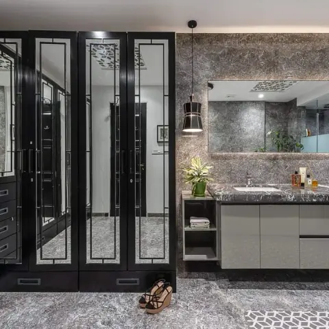 Twin-basin vanity under a long backlit mirror on grey-veined stone cladding, facing a wall of black lacquered wardrobes with mirrored shutters in slim deco