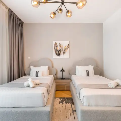 Twin-bed guest room with matching cloud-shaped upholstered headboards and a feather-print artwork centred between them, lit by a sputnik chandelier.