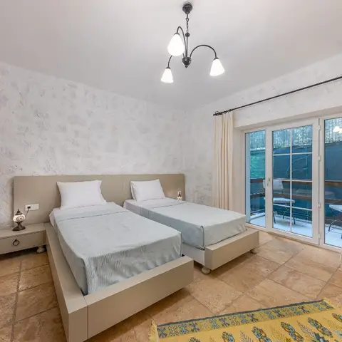 Twin-bed guest room with rustic textured stone-look walls, a wrought-iron chandelier, and glass doors opening onto a private balcony.