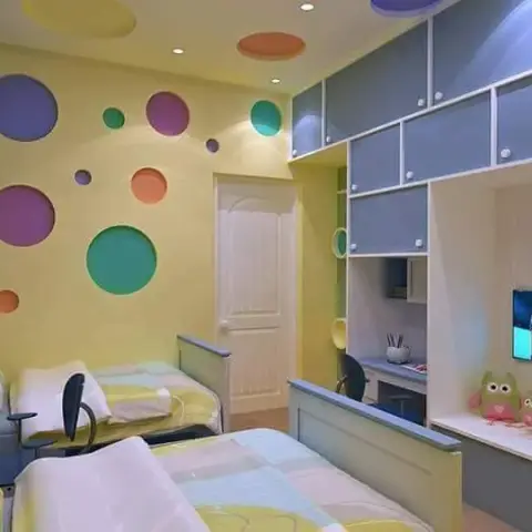 Twin-bed kids' room with a colourful cutout-circle feature wall and a blue built-in study desk beside a wall-mounted TV.