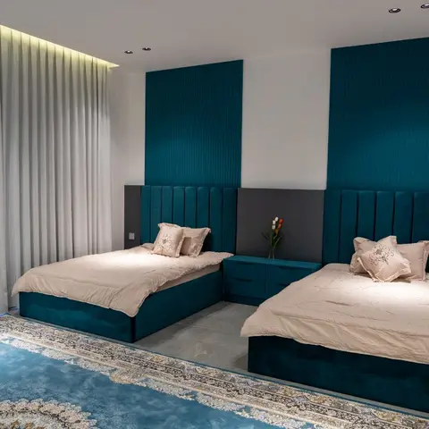Twin bedroom with matching teal channel-tufted beds set against fluted teal wall panels, a floating nightstand between them