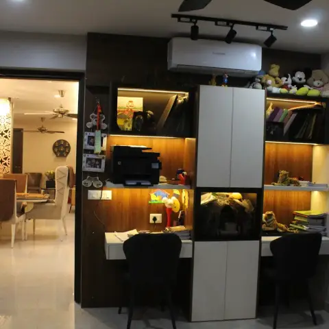 Twin built-in study desks flanking a tall white shutter column in a dark veneer wall, backlit shelves loaded with school files and stuffed tigers