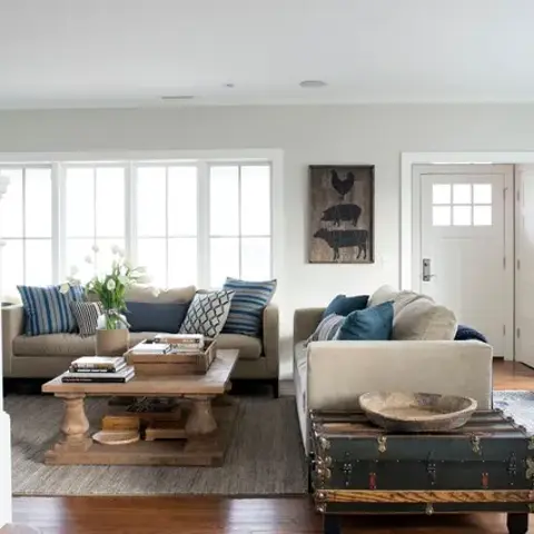 Two beige sofas facing across a chunky turned-leg timber coffee table on a jute rug, blue and striped cushions on both