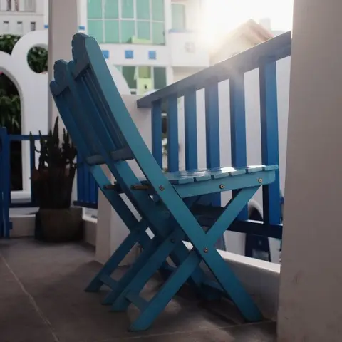 Two blue folding wooden chairs on a balcony with matching blue railings, an arched white doorway
