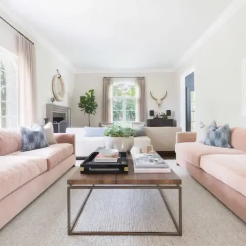 Two blush velvet sofas face each other across a walnut-and-brass coffee table on a sisal rug, with indigo tie-dye cushions