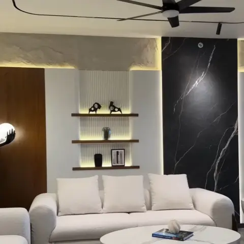 Two cream boucle sofas facing a round white pedestal coffee table, set between a full-height black-veined marble slab wall and a backlit fluted niche carrying