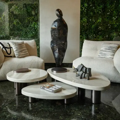 Two cream boucle sofas facing each other across three nesting stone-top tables on bronze cylinder legs