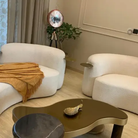Two curved cream boucle sofas with brass swing-out side trays face a kidney-shaped bronze-top coffee table