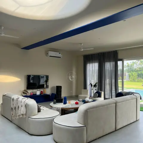 Two curved cream modular sofas facing each other under a sculpted ceiling with a circular skylight and a painted cobalt band