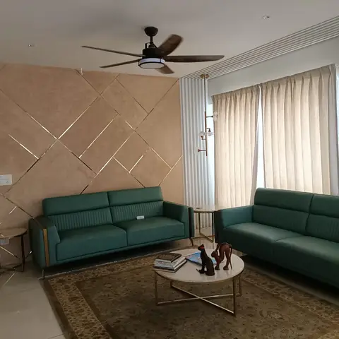 Two emerald green leather sofas facing a marble-and-gold coffee table, set against a peach diamond-quilted accent wall with brass inlay strips.