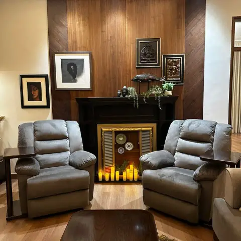 Two grey fabric recliners flank a black-mantel decorative fireplace filled with lit pillar candles