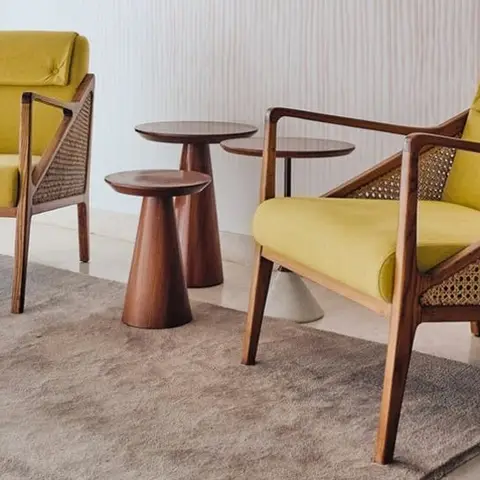 Two mustard-yellow rattan-back armchairs with wood frames flank a pair of round wood side tables on a grey rug