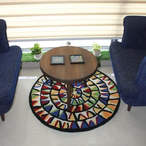 Two navy chenille armchairs face a round teak table holding a pair of framed Warli-style panels