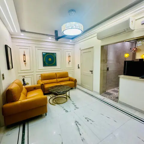 Two tan leather recliner sofas face a pair of gold-framed black marble nesting tables in a white living room, with moulded wall panels