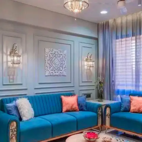 Two teal channel-tufted sofas with coral cushions on a crewel-embroidered floral rug, drawn around a round wooden drum table under a glass lantern chandelier