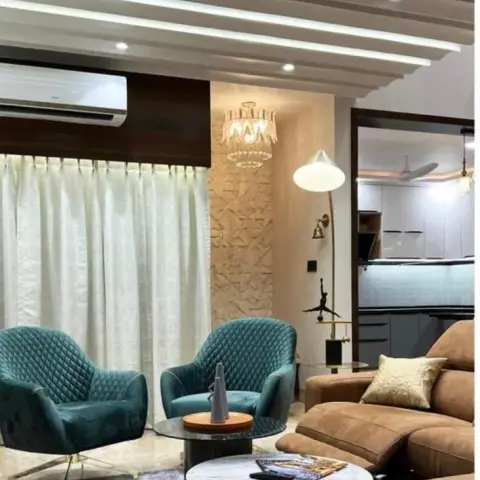 Two teal quilted-velvet swivel chairs on brass legs face a tan leather recliner sofa under a slatted fin ceiling