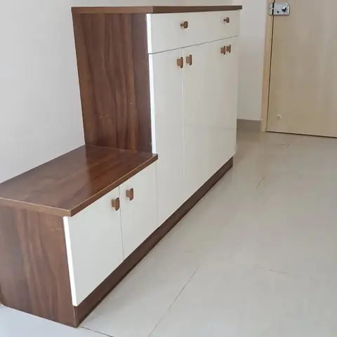 Two-tier laminate shoe/storage cabinet in white and wood-grain finish standing against a bare wall near the entrance door.