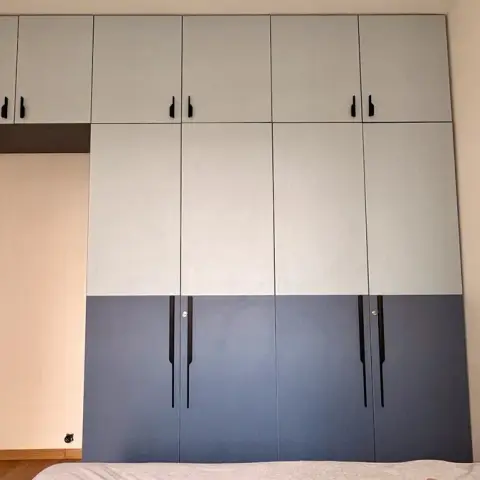 Two-tone wardrobe wall in pale grey over denim blue with long black bar handles and a full loft row