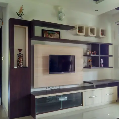 Two-tone wenge-and-maple laminate TV wall with a lit display niche holding a tall painted vase, three white wall cubes above and a glass-shuttered lower drawer.