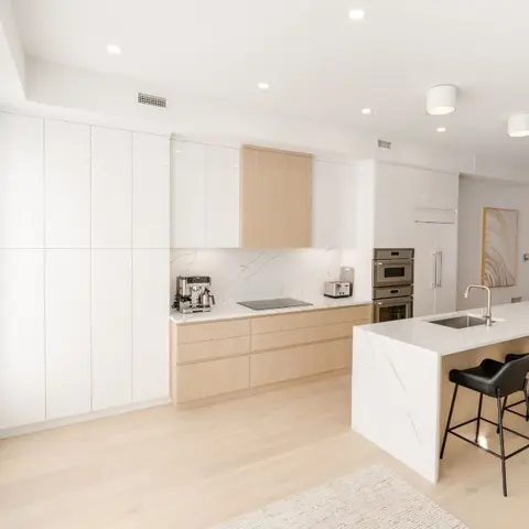 Two-tone white gloss and light oak kitchen with a marble waterfall island and black leather counter stools