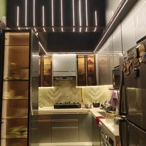 U-shaped kitchen at night in high-gloss taupe with copper-line handles, amber fluted-glass crockery units lit from inside